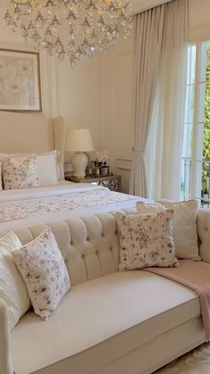 a large white bed sitting in a bedroom next to a chandelier and window