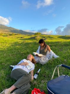 two women sitting in the grass reading and drinking