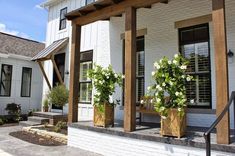 two wooden planters with white flowers are on the front porch of a house,