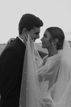 a man and woman standing next to each other with veils over their heads in black and white