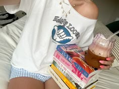 a woman sitting on a bed holding a drink and books