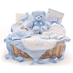 a blue teddy bear sitting in a wicker basket filled with baby clothes and blankets