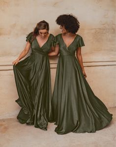 two women in green dresses standing next to each other with their hands on their hips