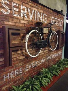 a bicycle mounted to the side of a brick wall that says serving good here everyday