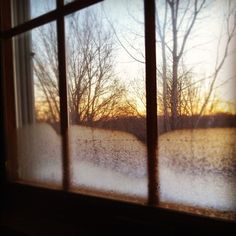 an open window with the sun setting in the background and snow on the ground outside