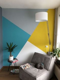 a cat sleeping on top of a gray chair in front of a wall with yellow and blue triangles