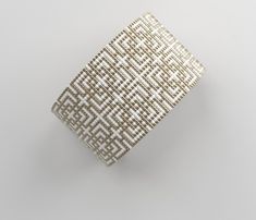 a white and gold bracelet with squares on it's sides, sitting on a gray surface