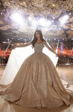 a woman in a gold and white gown is standing on the runway with her arms outstretched