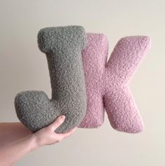 someone is holding two different colored pillows in the shape of letters k and person's hand