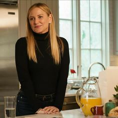 a woman standing in a kitchen next to a counter with orange juice and fruit on it