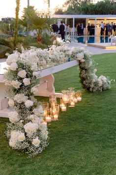 an outdoor ceremony setup with candles and flowers on the grass at dusk, in front of a pool