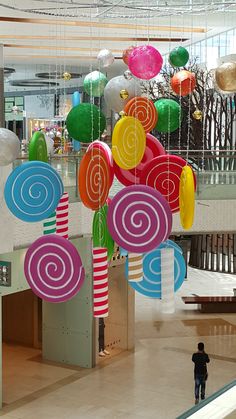 a man is standing in the middle of a mall with many colorful balloons hanging from it's ceiling