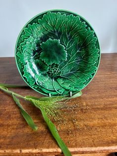 a green plate sitting on top of a wooden table next to a sprig of grass