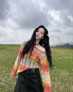 a woman standing on top of a lush green field next to a wind turbine in the distance