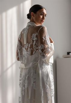 a woman standing in front of a window wearing a white dress with lace on it