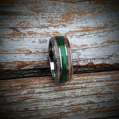 a wedding band with green and brown wood inlays on top of a wooden surface