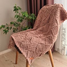 a chair that is made out of woven material and wooden legs, with a plant in the background