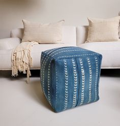 a blue ottoman sitting on top of a white floor next to a couch and pillows