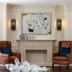 a living room with two brown chairs and a painting on the wall above it's fireplace