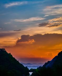 the sun is setting over some hills with trees on each side and clouds in the sky