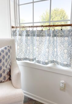 a white chair sitting in front of a window next to a blue and white curtain