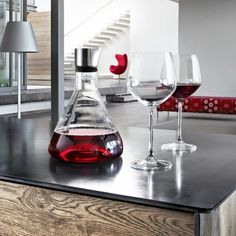 two wine glasses sitting on top of a counter next to a decanter filled with red liquid