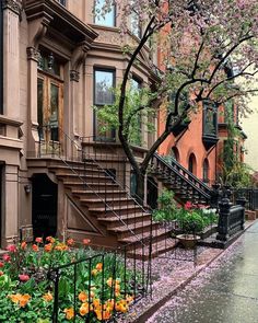 the flowers are blooming on the sidewalk in front of the brownstone building with wrought iron railings