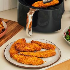 fried fish sticks on a plate next to a pot of fries and salad in bowls