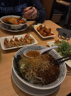 a bowl of noodles with chopsticks in it on a table next to plates of food