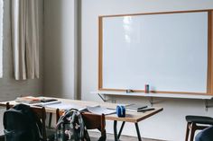 there is a white board on the wall next to two chairs and a backpack in front of it