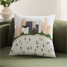 a pillow on a couch with people skiing in the snow and cityscape behind it