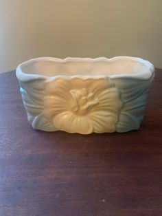 a white flowered bowl sitting on top of a wooden table next to a wall