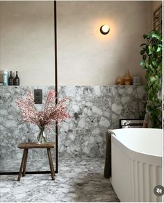 a white bath tub sitting next to a wooden stool in a room with marble walls