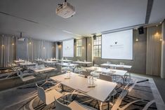 an empty room with tables and chairs in front of a projector screen on the wall