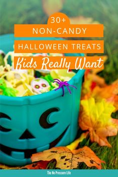 a blue bowl filled with halloween treats sitting on top of green grass next to leaves