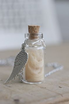 an angel wing charm sits in a glass bottle on a wooden table with a chain around it