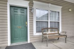 a bench sitting in front of a green door next to a window on a house