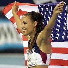 a woman holding an american flag in front of her chest and arms, with both hands up