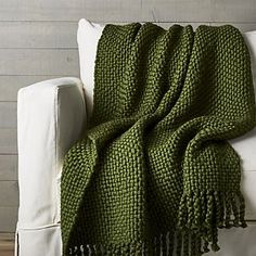 a green knitted blanket sitting on top of a white couch next to a pillow