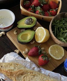 an assortment of fruits, vegetables and bread on a cutting board next to bowls of nuts