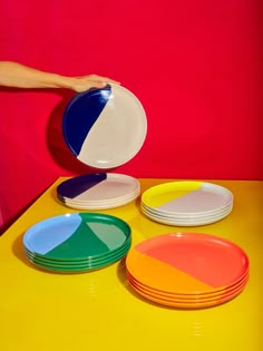 a person holding a plate in front of several plates on a yellow and red table