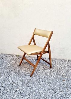 a wooden chair sitting on top of a gravel covered floor next to a white wall