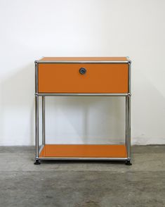 an orange and chrome end table with two drawers on each side, against a white wall