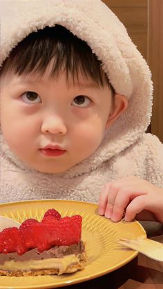 a young child wearing a white robe and holding a plate with some food on it