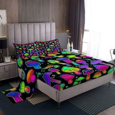 a bed covered in colorful sheets and pillows next to a night stand with a lamp on it