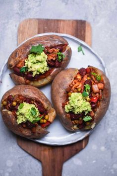 three loaded baked potatoes on a plate with guacamole and cilantro