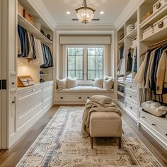 a large walk in closet with lots of clothes on hangers and drawers, along with a bench