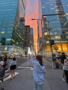 a woman taking a photo in the middle of a busy city street at sunset with tall buildings