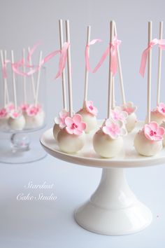 cake pops decorated with pink flowers and ribbons on a white platter, ready to be eaten