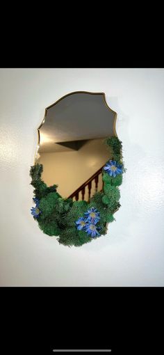 a mirror that is on the wall with blue flowers in front of it and a stair case behind it